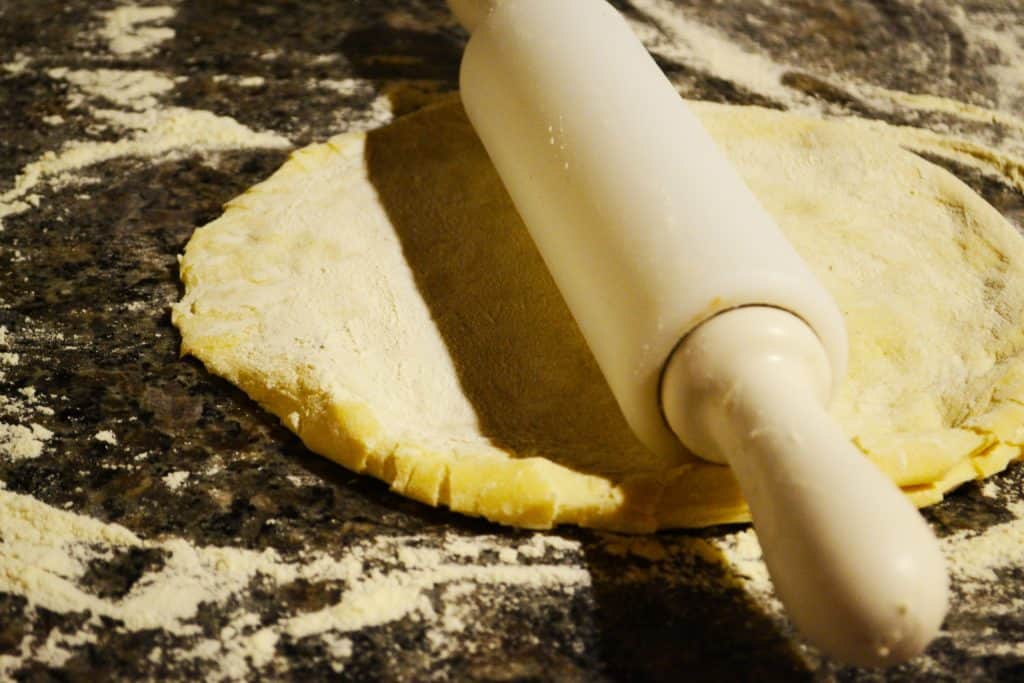 Dough on a floury surfaced being rolled out with a rolling pin