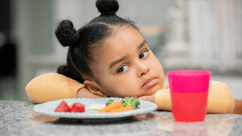 Young girl sat at the table refusing to eat her food