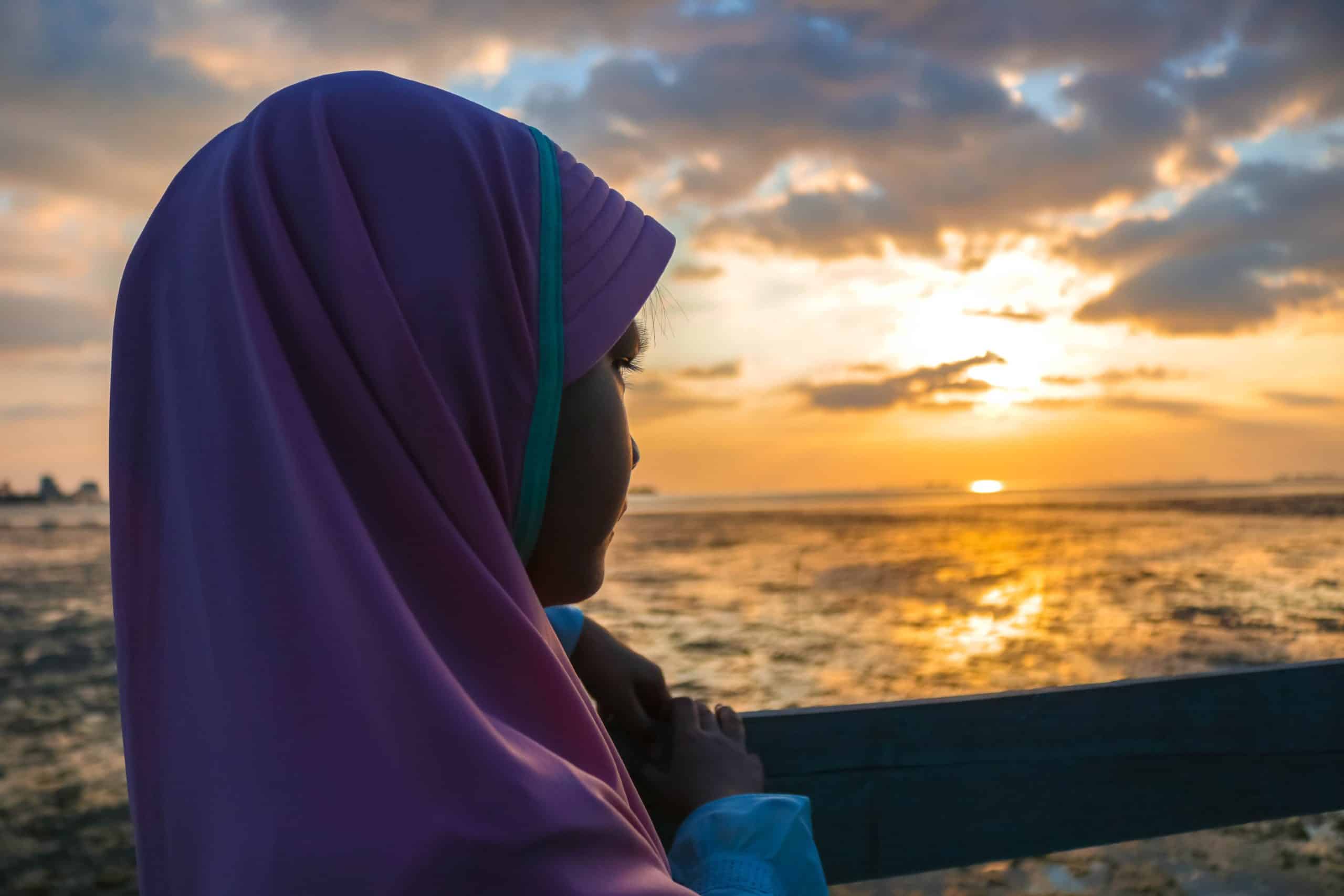 Girl wearing a hijab looking towards the setting sun