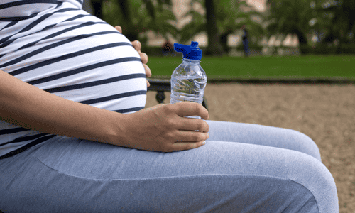 Pregnant woman drinking water in the park