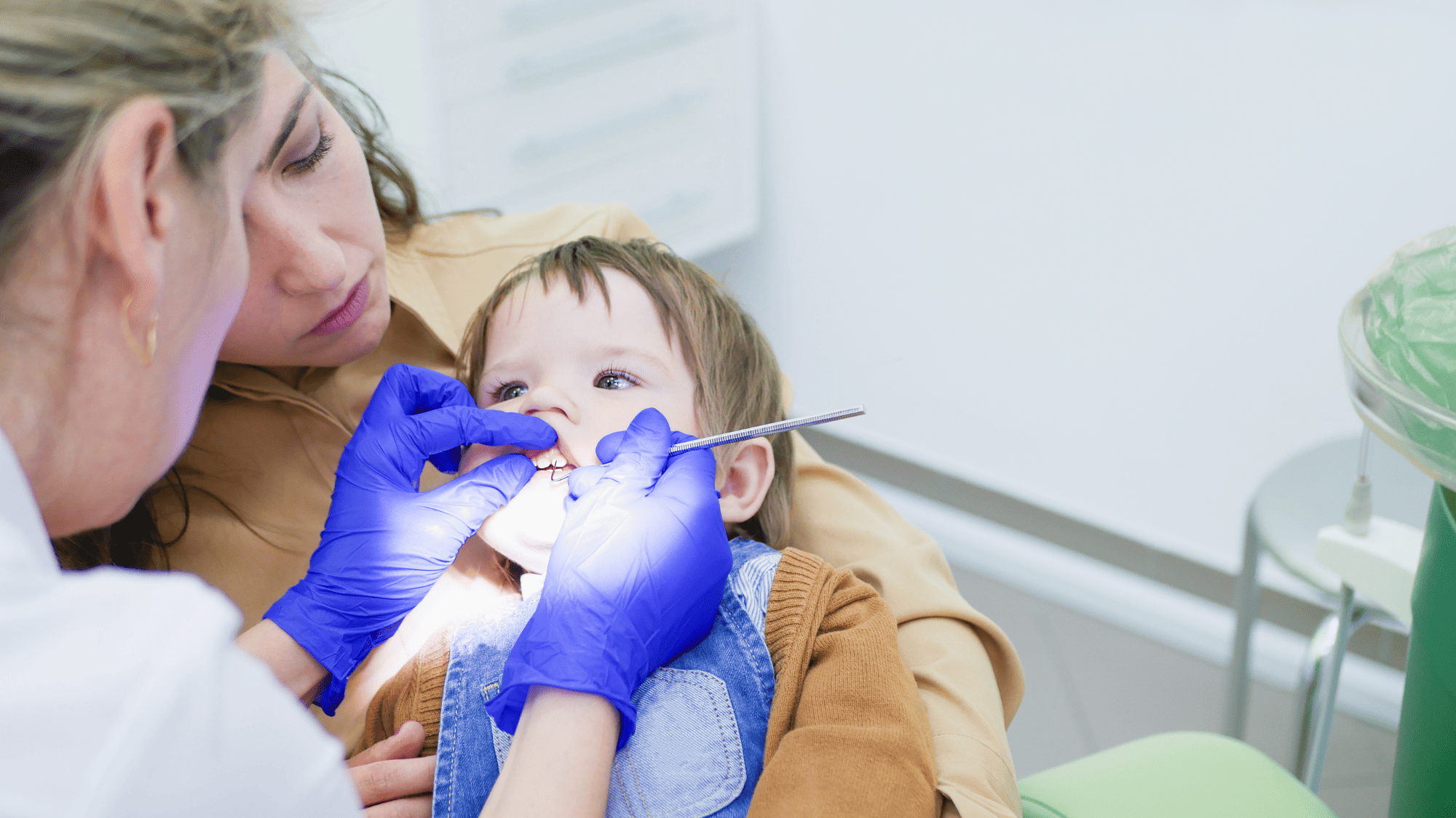 Young Child Visiting the Dentist, sat on her mothers lap, while the dentist looks at her teeth
