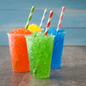 Four slush-ice drinks in plastic cups with straws. They are coloured orange, green, blue, yellow